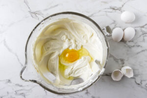 Adding eggs to the cheesecake bar filling.