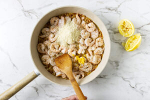 Shrimp arranged over orzo while cooking in a skillet.