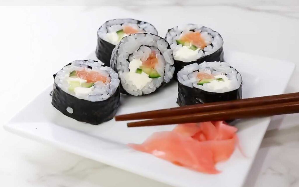 Several slices of salmon cream cheese sushi on a plate with pickled ginger.