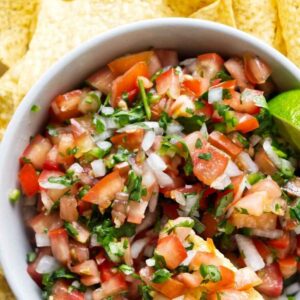 Hand holds chip with pico de gallo over bowl, chips surrounding.