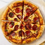 Pepperoni pizza with melted cheese and herbs on parchment paper.