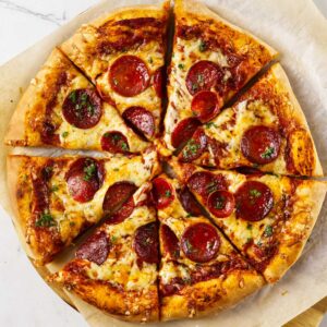 Pepperoni pizza with melted cheese and herbs on parchment paper.