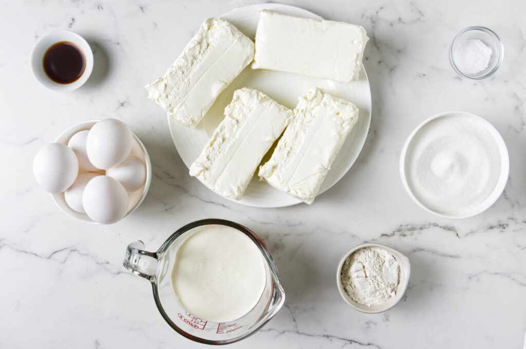 Assorted cheesecake ingredients arranged on a marble countertop.