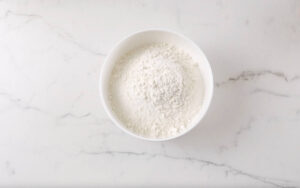 White bowl of flour on a white marble countertop.