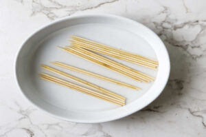 Wooden skewers soaking in water in a white oval dish.
