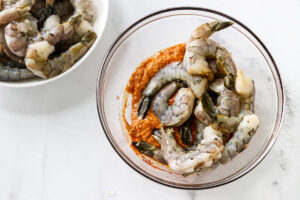 Peeled shrimp added to smoky garlic marinade in a mixing bowl.
