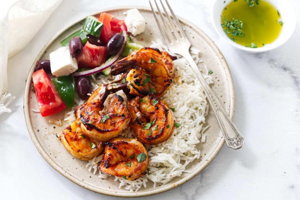 Plate of spicy shrimp skewers with rice, salad, and lemon butter.