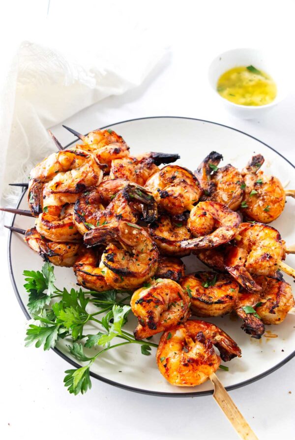 Vertical image of spicy grilled shrimp skewers served with lemon parsley butter.