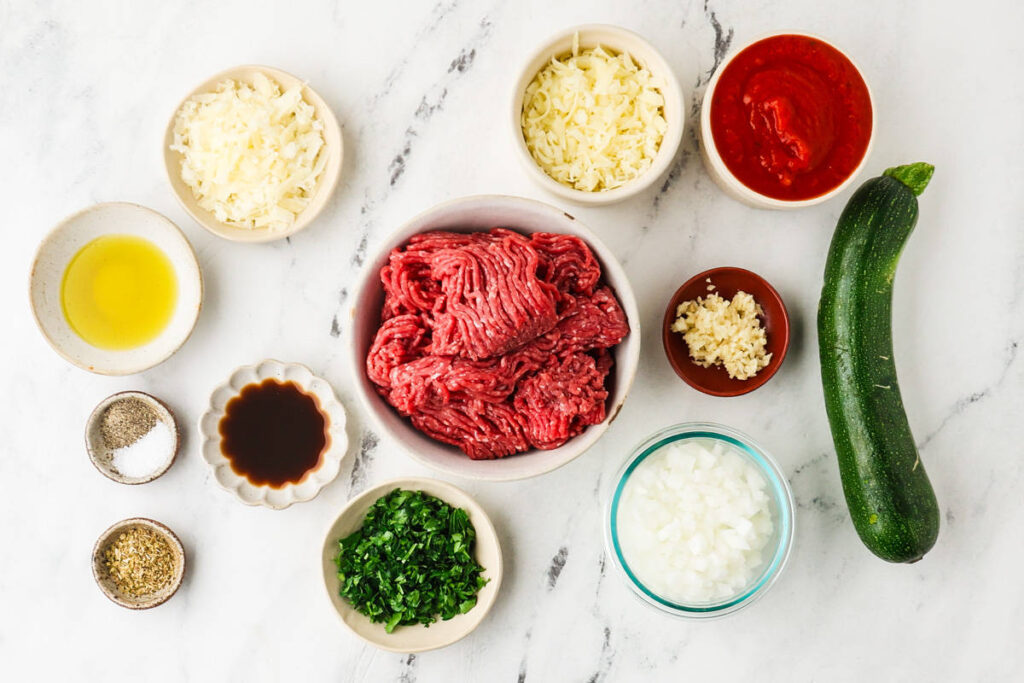 Ingredients for stuffed zucchini boats with ground beef, cheese, marinara, and herbs.