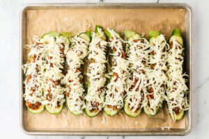 Unbaked zucchini boats filled with meat sauce and topped with shredded mozzarella.