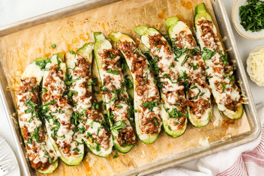 Finished zucchini stuffed with ground beef filling on a parchment-lined sheet pan.