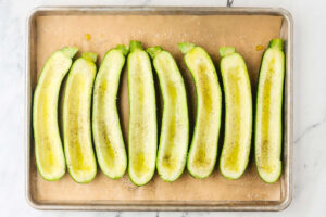 Scooped zucchini halves brushed with olive oil on a baking sheet.