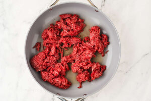 Raw ground beef in a skillet for zucchini boat filling.