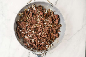 Ground beef mixture cooking with onion for stuffed zucchini boats.