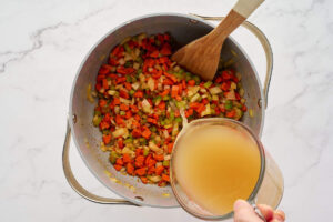 Chicken broth being poured over sautéed vegetables for Italian wedding soup.