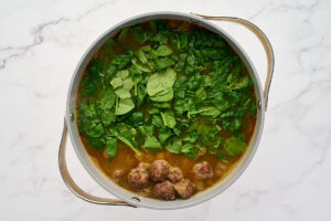 Italian wedding soup in a pot with meatballs and chopped greens added to the broth.