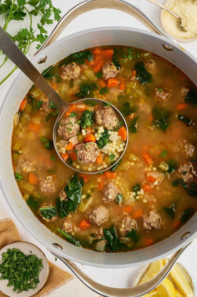 Top-down view of Italian wedding soup cooking in a pot with meatballs, vegetables, and greens.