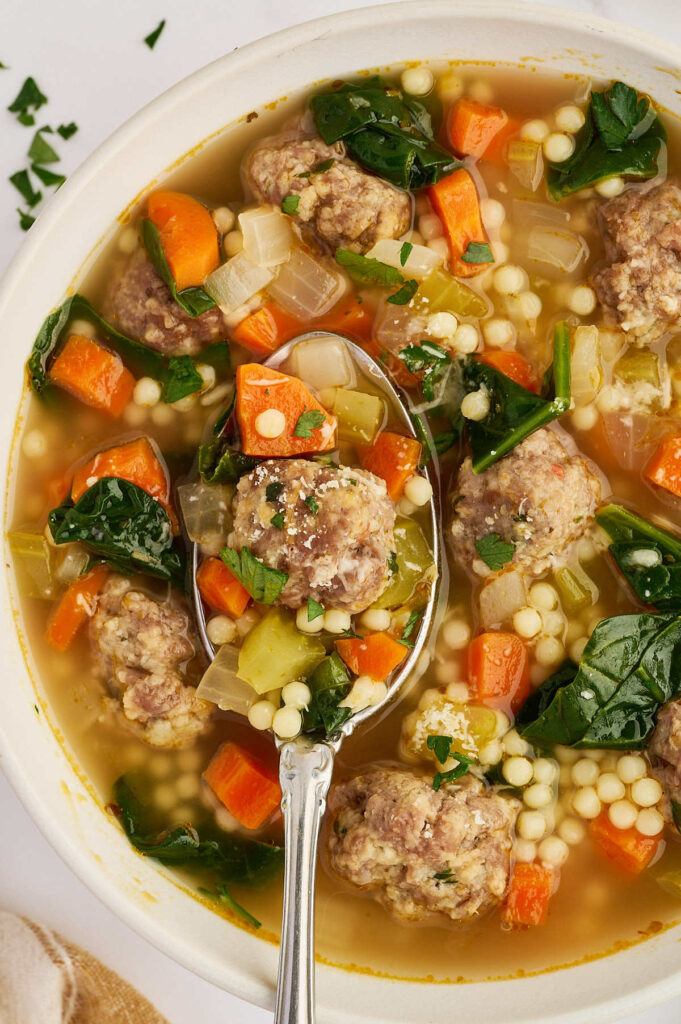 Vertical view of a bowl of Italian wedding soup filled with meatballs, spinach, carrots, and pasta.