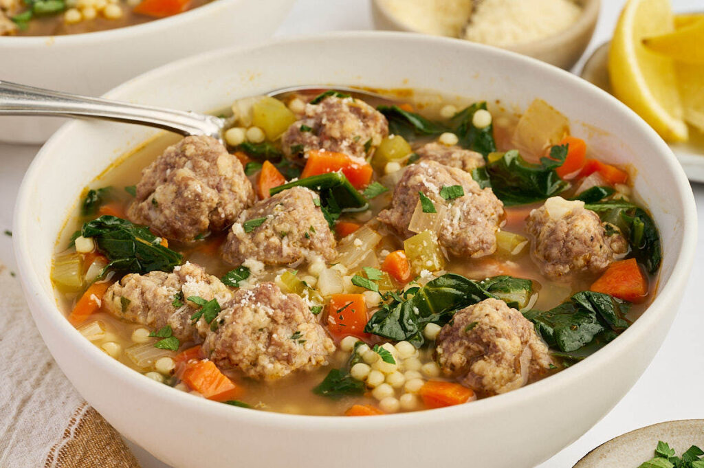 Italian wedding soup with baked meatballs and vegetables served in a white bowl.