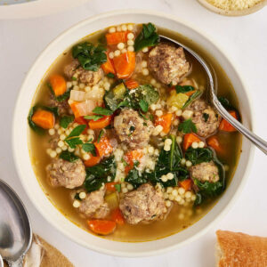 Overhead bowl of homemade Italian wedding soup with meatballs, spinach, carrots, celery, acini di pepe, and a spoon.