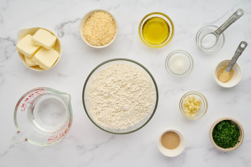 Ingredients for homemade garlic knots with flour, yeast, olive oil, butter, garlic, Parmesan, and parsley.