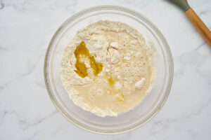 Flour, yeast, water, and olive oil in a mixing bowl for garlic knot dough.