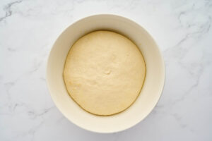 Risen garlic knot dough in a white bowl after the first rise.