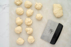 Portioned dough pieces for homemade garlic knots beside a bench scraper.