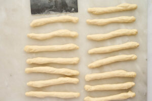 Dough ropes arranged on parchment paper for shaping homemade garlic knots.