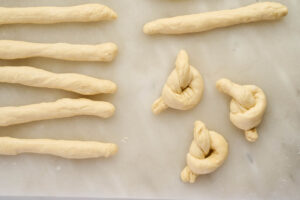 Pizza dough ropes tied into garlic knots on a floured work surface.