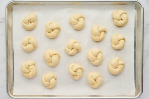 Risen garlic knots arranged on a parchment-lined baking sheet before baking.