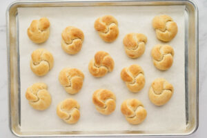 Plain baked garlic knots on a parchment-lined sheet pan before adding garlic butter.