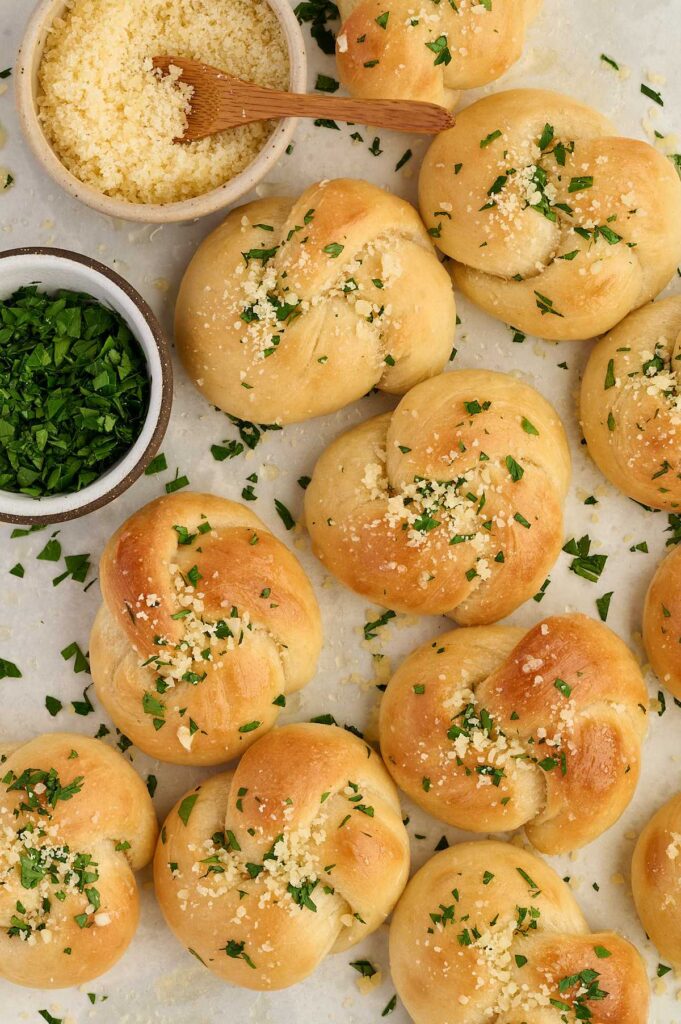 Vertical image of homemade garlic knots with marinara, garlic butter, and fresh parsley.