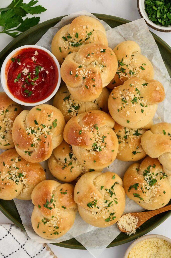 Overhead platter of garlic knot bread with marinara sauce for serving.