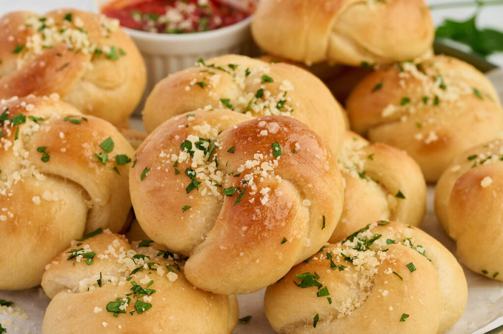Close-up of soft garlic knot bread brushed with butter, Parmesan, and parsley.