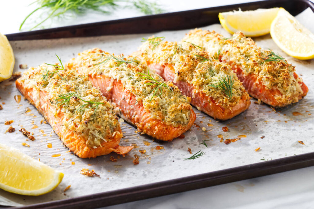 Garlic Parmesan crusted salmon fillets with lemon wedges on a baking sheet.
