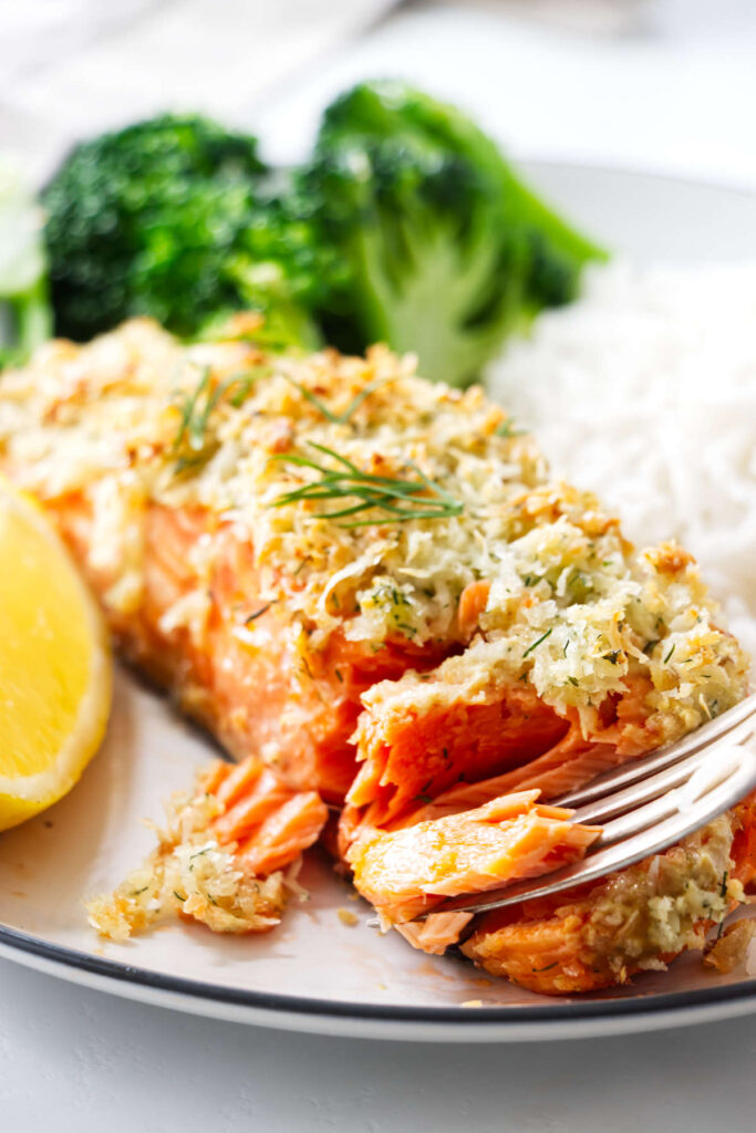 Breaded baked salmon flaked with a fork on a plate with broccoli and lemon.