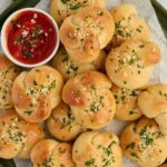 Homemade garlic knots on a platter with marinara sauce for dipping.