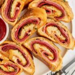 Sliced stromboli with deli meats on white plate, marinara sauce beside.