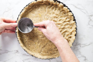 Pressing a nut crust mixture into a tart pan.