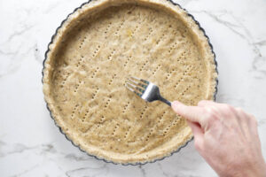 Hand poking holes in unbaked pie crust with fork on countertop.