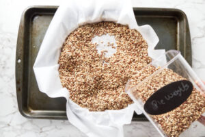 Pie weights being poured into a parchment-lined crust on a baking tray.