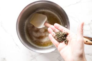 Adding chopped rosemary to a saucepan with browned butter.