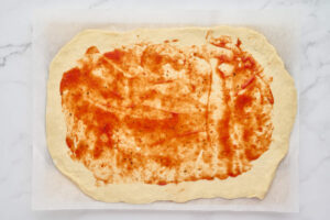 Pizza sauce spread over stromboli dough, leaving a border around the edges.