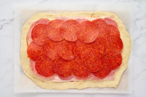 Pepperoni layered over salami and ham on a rectangle of stromboli dough.