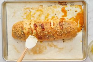 Baked stromboli on a sheet pan being brushed with garlic butter.