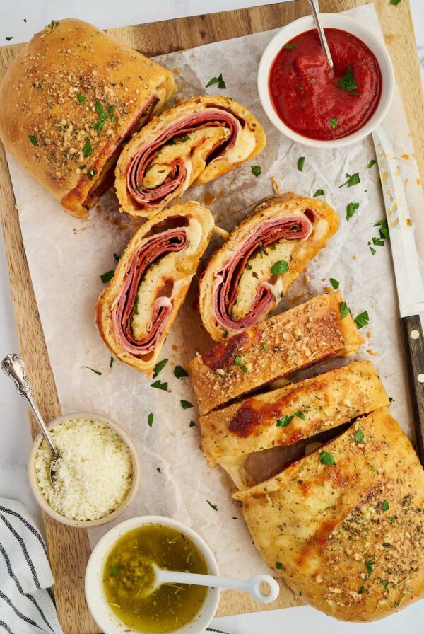 Homemade stromboli with a sliced piece and marinara sauce on parchment paper.
