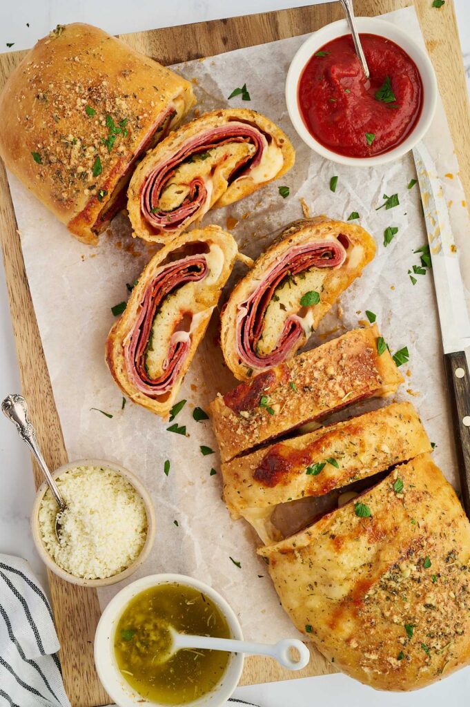 Homemade stromboli with a sliced piece and marinara sauce on parchment paper.