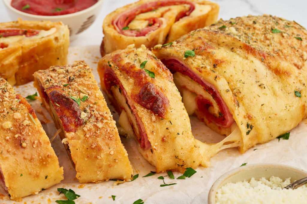 Baked pepperoni stromboli sliced into thick pieces with marinara for dipping.