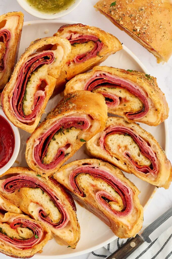 Sliced meat stromboli arranged on a platter with marinara sauce and garlic butter.